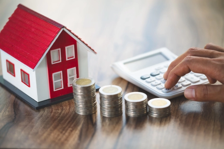 Maqueta de vivienda, monedas y calculadora sobre una mesa