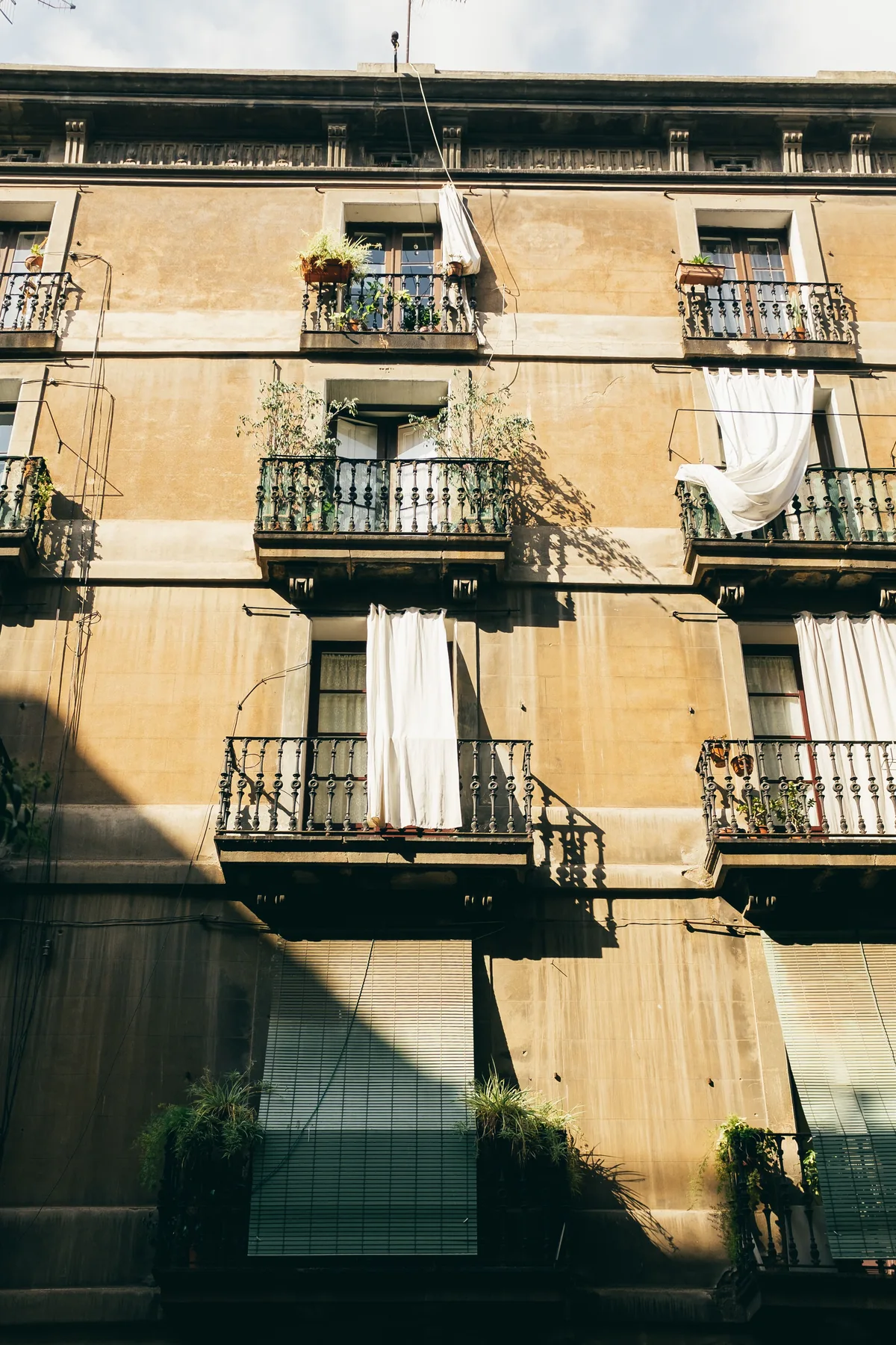 Façana d’un edifici residencial de Barcelona amb balcons, plantes i cortines blanques